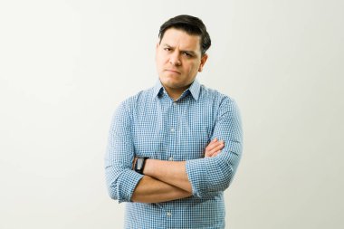 Profesyonel iş adamı kollarını kavuşturmuş, mavi kareli gömleğiyle tarafsız stüdyo geçmişine karşı çıkıyor.