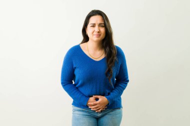 Şiddetli karın ağrısı çeken genç bir kadın, kederli bir ifadeyle karnını tutuyor.