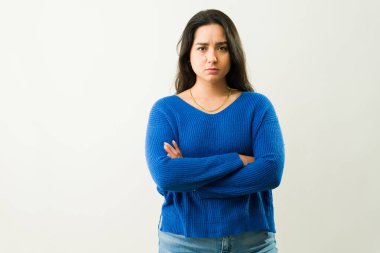 Kollarını kavuşturup beyaz bir arkaplanda onaylamayan Latin kökenli genç bir kadının stüdyo portresi