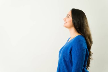 Mavi örgü süveter giyen neşeli bayan profesyonel, kendine güvenerek ışıldıyor ve el değmemiş arka plana doğru bakıyor.