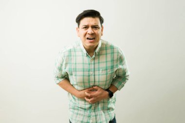Keskin karın krampları çeken bir erkek, karnını sıkıyor ve şiddetli gastrointestinal sıkıntıdan ürküyor.
