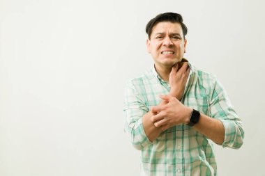 Alerjiden muzdarip bir adam kaşındıran derisini kaşıyarak ve ağrıyan boğazına alerjik reaksiyon yüzünden acı veren bir ifadeyle dokunuyor.