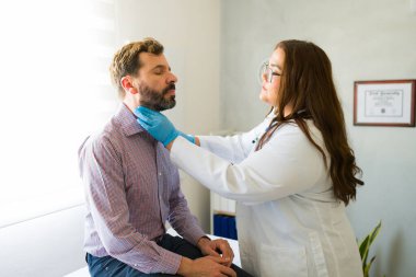 Tıbbi uzman, rutin sağlık kontrolü sırasında hastanın boynunu muayene ediyor, elle muayene tekniğiyle fiziksel değerlendirme yapıyor.