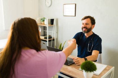 Erkek doktor, kadın hastayı selamlıyor. Profesyonel sağlık hizmetlerindeki olumlu tıbbi muayeneden sonra sıcak bir şekilde el sıkışıyor.
