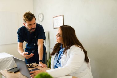 Tıbbi uzmanlar, bir dizüstü bilgisayar kullanarak hasta verileri üzerinde işbirliği yapıyor, bir doktorun ofisinde takım çalışması ve dijital sağlık hizmetlerini ön plana çıkarıyor
