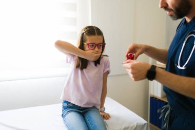 Erkek doktor, bir doktorun muayenehanesinde otururken ağzını kapatan genç bir kadın hasta için ilaç hazırlıyor.