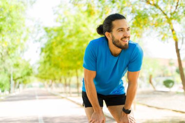 Parktaki bir pistte dinlenen mutlu sporcu canlandırıcı bir koşudan sonra güneşli bir günün tadını çıkarıyor, sağlık ve zindeliği kucaklıyor.