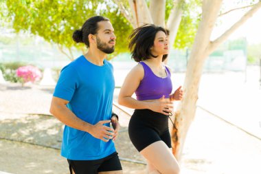 Genç İspanyol çift parkta koşuyor, antrenmanlarının tadını çıkarıyor ve sağlıklı bir yaşam tarzı geliştiriyor.