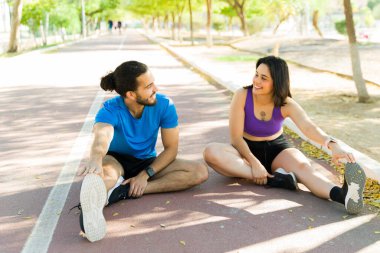Koşucular hareketli bir koşu pistinde antrenman yaptıktan sonra bacaklarını uzatıp gülümseme paylaşıyorlar. Spor ve birlikte havanın tadını çıkarıyorlar.