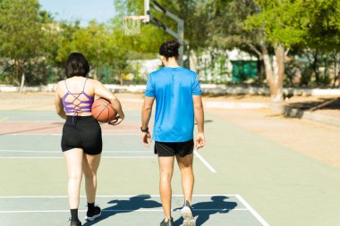 Güneşli bir günde maç yaptıktan sonra basketbol sahasında yürüyen bir çiftin arka görüntüsü.