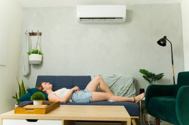 Sıcak bir yaz gününde, sıcak bir kanepede dinlenen ve klimanın serin havasının tadını çıkaran bir kadın.