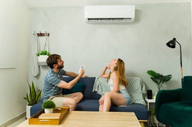 Genç bir çift kanepede oturuyor, uzaktan kumandayı çalıştırıyor, sıcak bir yaz gününde klimanın serin havasının tadını çıkarıyorlar.