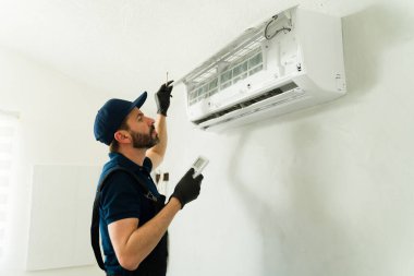 Hvac teknisyeninin uzaktan kumanda kullanarak ve eldiven ve üniforma giyerek havalandırma ünitesinde çalıştığını gösteren profil görüntüsü