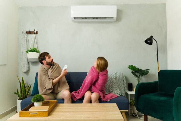 Man and woman wrapped in blankets, freezing and arguing about the temperature set on the air conditioner
