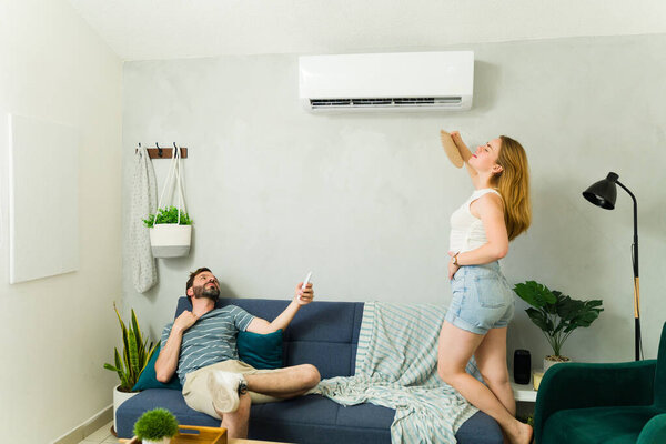 Sad couple suffering from the heat while turning on the air conditioning from mini split unit on a hot summer day
