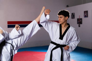 İki sporcu tekvando çalışıyor, biri yüksek tekme atıyor, diğeri ise bu dövüş sanatlarının hareketlerini gösteriyor.