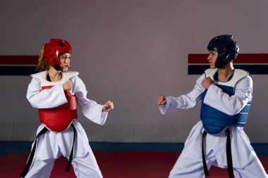 İki sporcu tekvando antrenmanı yapıyor koruyucu kıyafetler giyip dövüş sanatları becerilerini sergiliyorlar.