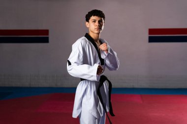Genç atlet tekvando çalışıyor. Dobok ve siyah kuşak takıyor. Spor salonunda dövüş sanatları yapıyor.
