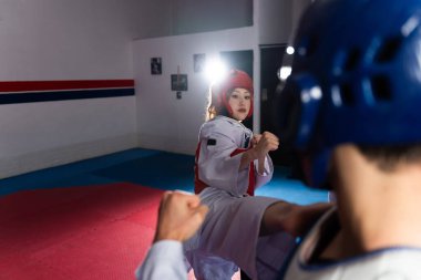 İki sporcu, tekvando antrenmanında rakibini tekmeleyen bir kadın dövüşçüyle dövüşüyor.