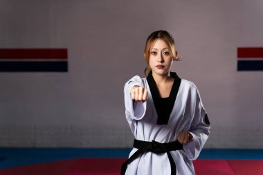 Dobok ve siyah kuşak giyen bayan sporcu bir spor salonunda tekvando antrenmanı sırasında savunma hareketi yapıyor.