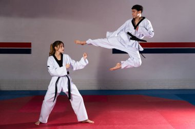 Dövüş sanatları atletleri tekvando çalışıyor kırmızı ve mavi paspaslarla bir spor salonunda uçan tekme atıyorlar.