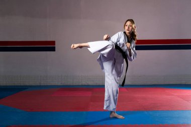Siyah kuşaklı bir kadın spor salonunda güçlü bir tekvando tekmesi atıyor. Gücünü, yeteneğini ve kararlılığını gösteriyor.