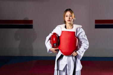 Kendine güveni tam bir bayan atlet. Dobok giyiyor ve koruyucu giysiler giyiyor. Dövüş sanatları eğitiminde güç ve beceri sergiliyor.