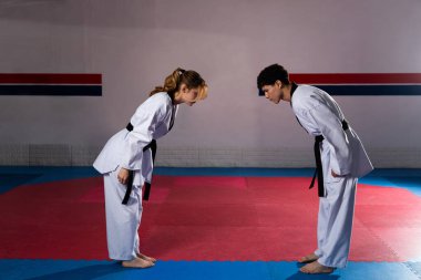 Beyaz üniformalı ve siyah kuşaklı iki dövüş sanatları dövüşçüsü spor salonunda kırmızı ve mavi bir paspasın üzerinde eğiliyor.