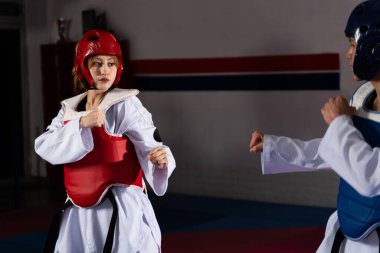 Tekvando antrenmanı yapan sporcular, koruyucu giysi ve doboks giyiyorlar, bir spor salonunda idman maçı yapıyorlar.