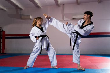 İki yetenekli tekvando atleti, doboks ve siyah kemer takan bir erkek ve bir kadın, dövüş sanatları teknikleri üzerinde idman yapıyorlar.