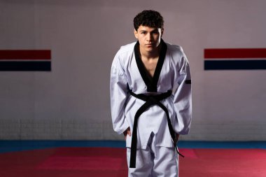 Ciddi genç erkek sporcu tekvando salonunda eğiliyor. Dövüş sanatlarında saygı ve disiplin gösteriyor.