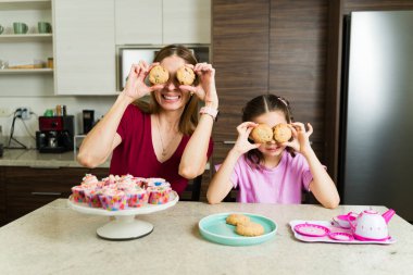 Mutfakta kurabiye pişirirken ellerinde kurabiyelerle neşeli bir anne ve kız.