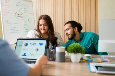 Çeşitli pazarlama ekibi, ofis toplantısı sırasında dizüstü bilgisayardaki müşteri verilerini analiz ediyor, satış kanallarını ve işbirliğini tartışıyor.