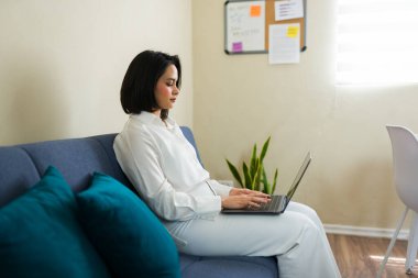 Genç girişimci çevrimiçi işine odaklanmış, ev ofisinden uzakta rahat bir şekilde çalışıyor.