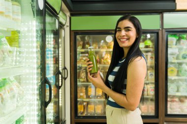 Süpermarketten alışveriş yaparken elinde bir şişe yeşil meyve suyu tutan mutlu Latin müşteri.