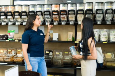 Sıfır atık dükkanından ürün seçen, sürdürülebilir alışverişin faydalarını açıklayan ve çeşitli ürünleri gösteren bir mağaza asistanı