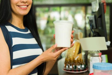 Gülümseyen bir kadın markette elinde beyaz yoğurt kabıyla arka planda diğer gıda ürünlerini tutuyor.