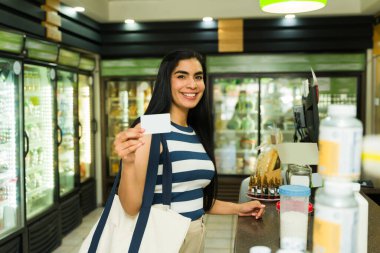 Neşeli İspanyol kadın, markette kredi kartını gösterirken gülümsüyor, evi için alışveriş yapıyor.