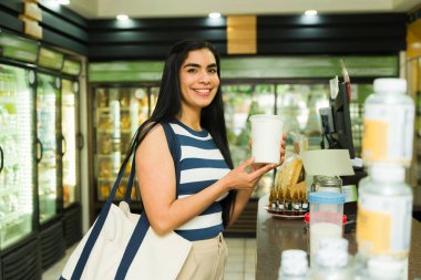 Neşeli Latin müşteri marketten alışveriş yaparken yoğurt konteynırını tutuyor.