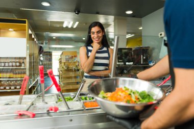 Neşeli müşteri salata barında sağlıklı yemek sipariş ediyor ve yemeği için taze malzemeler seçiyor.