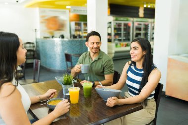 Mutlu bir Latin arkadaş grubu sağlıklı bir öğle yemeğinin tadını çıkarıyor, salata yiyor ve modern bir restoranda meyve suyu içiyor.