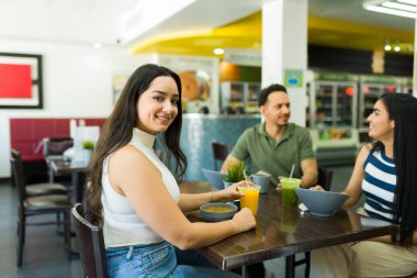 Bir grup Latin arkadaş sağlıklı bir öğle yemeğinin tadını çıkarıyor, salata yiyor ve bir restoranda meyve suyu içiyor.
