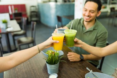 Bir grup arkadaş bir restoranda sağlıklı bir öğle yemeğinin tadını çıkarırken renkli meyve sularıyla kadeh kaldırıyoruz.