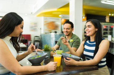 Bir grup mutlu genç iş arkadaşı birlikte sağlıklı bir öğle yemeği arası veriyor, taze salata yiyor ve restoranda sohbet ediyorlar.