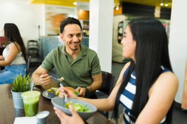 İspanyol adam ve kadın taze salata ve burger yiyor, sağlıklı bir öğle yemeği yiyor ve restoranda sohbet ediyorlar.