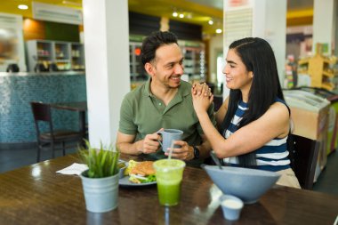 Neşeli İspanyol adam ve kadın bir restoranda sağlıklı bir öğle yemeğinin tadını çıkarıyor, el ele tutuşuyor ve iyi vakit geçiriyorlar.