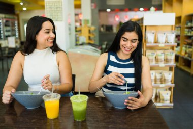 İki genç İspanyol kadın sıcak bir restoranda sohbet ederken ve gülümserken taze salata ve ferahlatıcı meyve suyu ile canlı bir öğle yemeğinin tadını çıkarıyorlar.