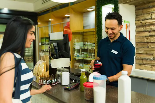 Dost canlısı kasiyer bakkaliyeleri kasada barkod tarayıcı ile tarıyor, süpermarketteki kadın müşterilere verimli ve uygun hizmet sunuyor