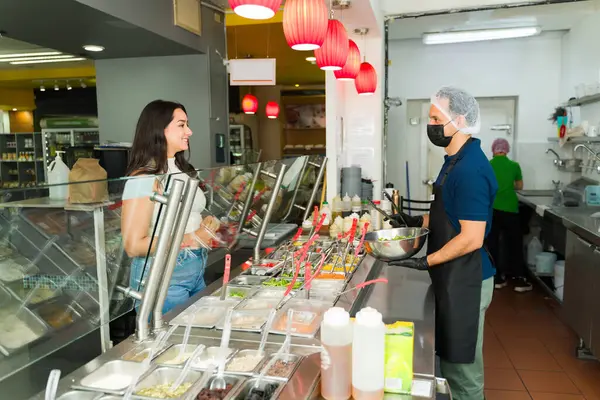 Restoran çalışanı salata tezgahında canlı, sağlıklı bir salata hazırlıyor. Kadın müşteriye taze malzemeler servis ediyor.