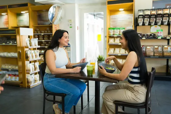 İki mutlu kadın taze salata yiyor ve bir restoranda konuşurken ve yemek yerken sağlıklı içecekler içiyorlar.
